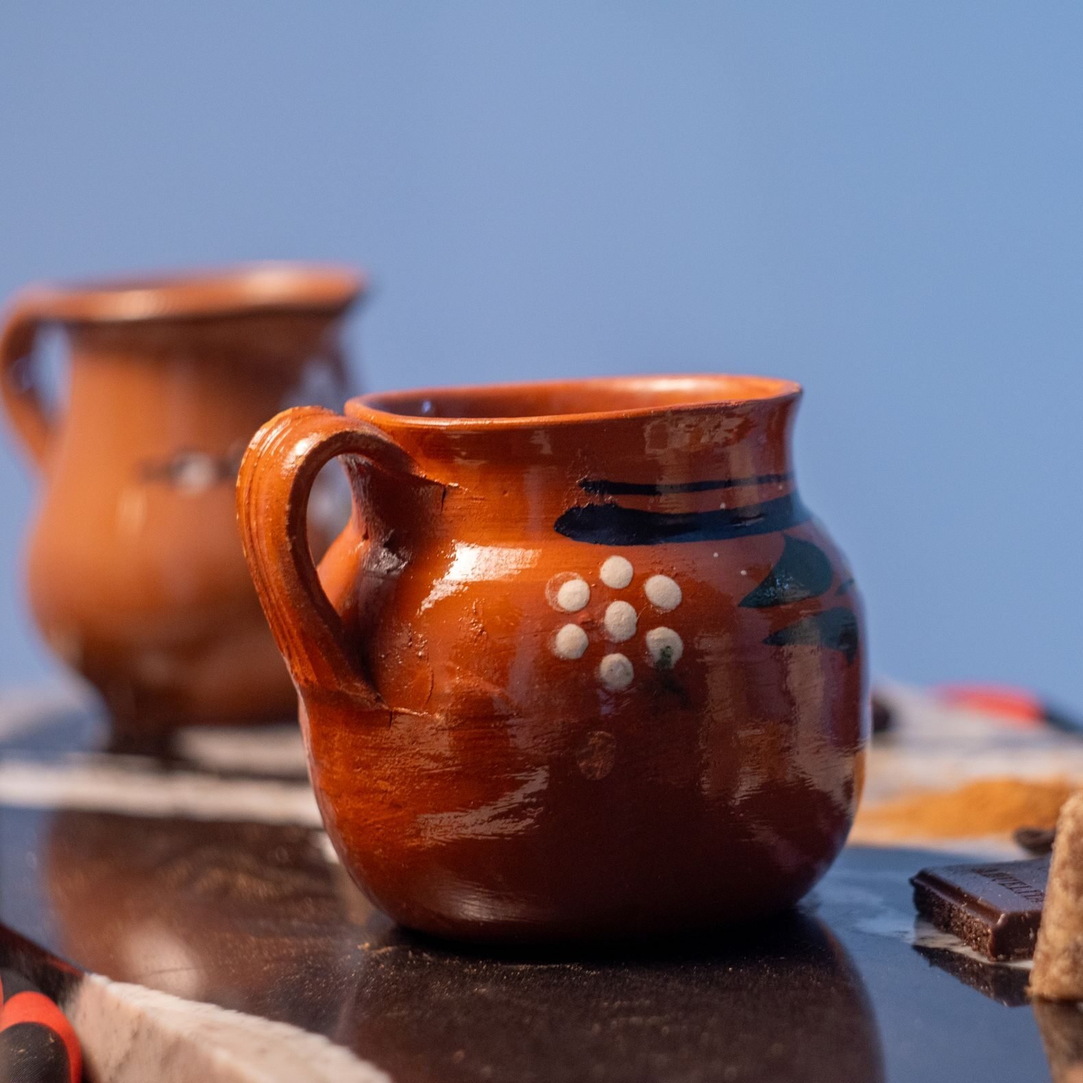 Close-up of traditional Mexican clay mugs with coffee and spices, showcasing cafe de olla.